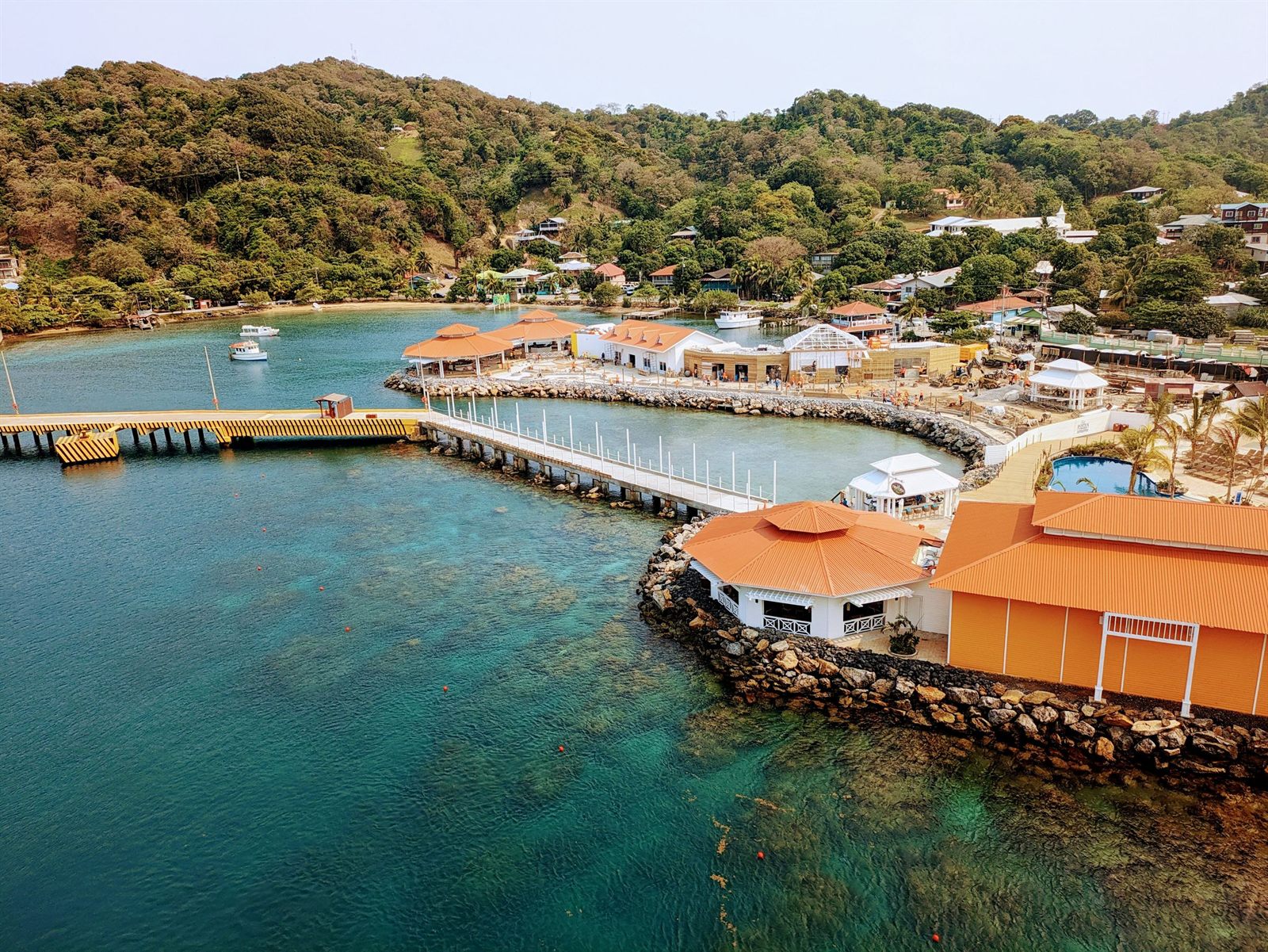 Aerial view of a cruise pier and orange-roofed port buildings on the green coast of Roatan